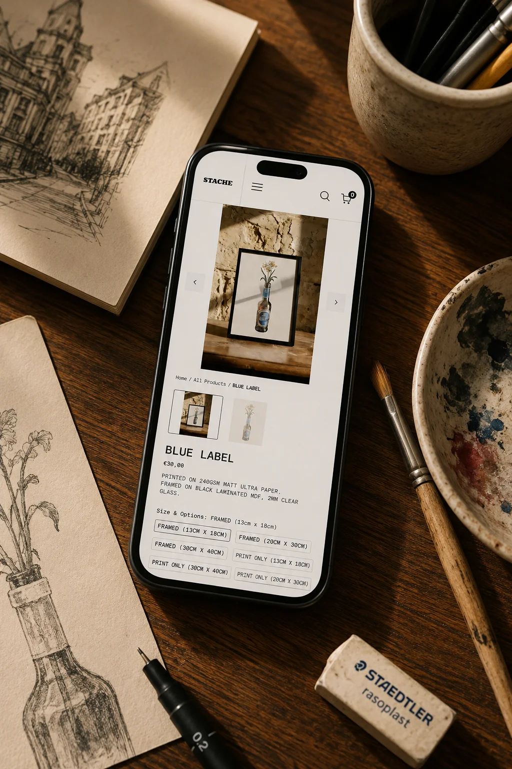 The Blue Label product page on mobile. The framed print is photographed on a rustic wooden table against an exposed limestone wall. Below the hero photo, a thumbnail gallery, the product title and price 30 euros, a paper and frame spec line, and a Size and Options variant picker with six choices spanning framed and print-only formats at three sizes each.